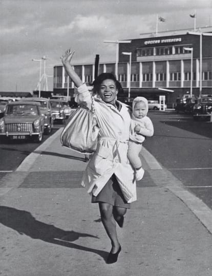 A joyful woman waving and carrying a child, capturing the welcoming and cheerful atmosphere of the baby club class.